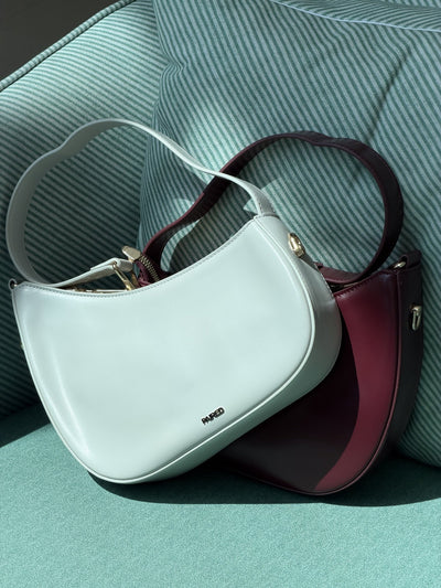 Paired Clarissa Chain Bag in white and burgundy lying together on a teal armchair, with straps and chain links