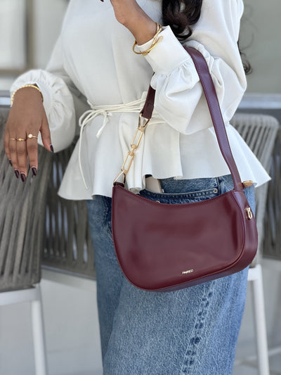 Paired Clarissa Chain Bag in burgundy, worn on the shoulder with a flat strap, with a white blouse and wide-leg jeans