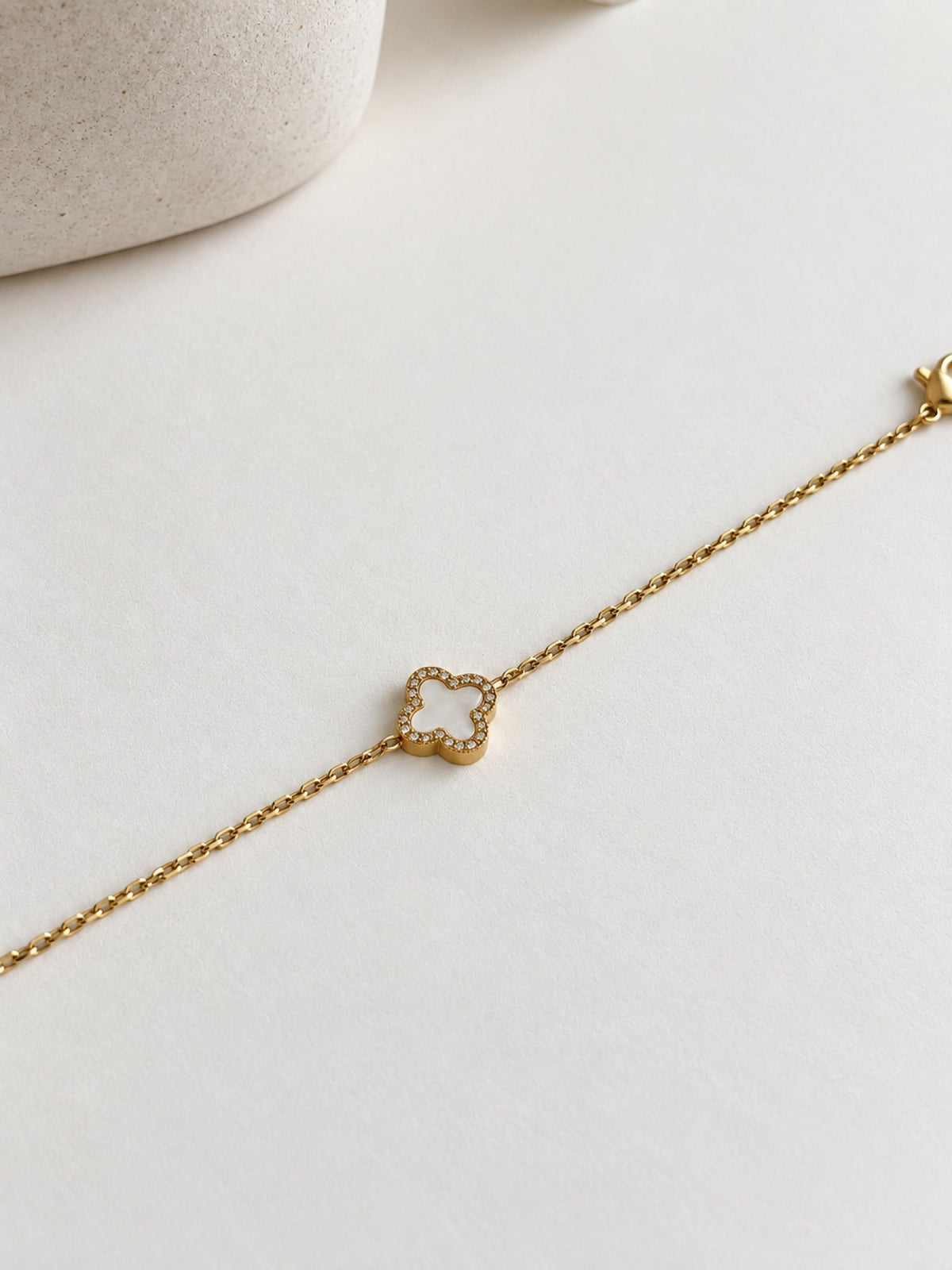 Paired Clover Étoile Bracelet in gold-tone, laid flat on a cream surface with its white clover charm and fine chain