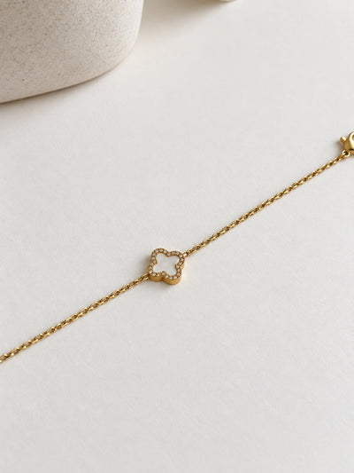 Paired Clover Étoile Bracelet in gold-tone, laid flat on a cream surface with its white clover charm and fine chain