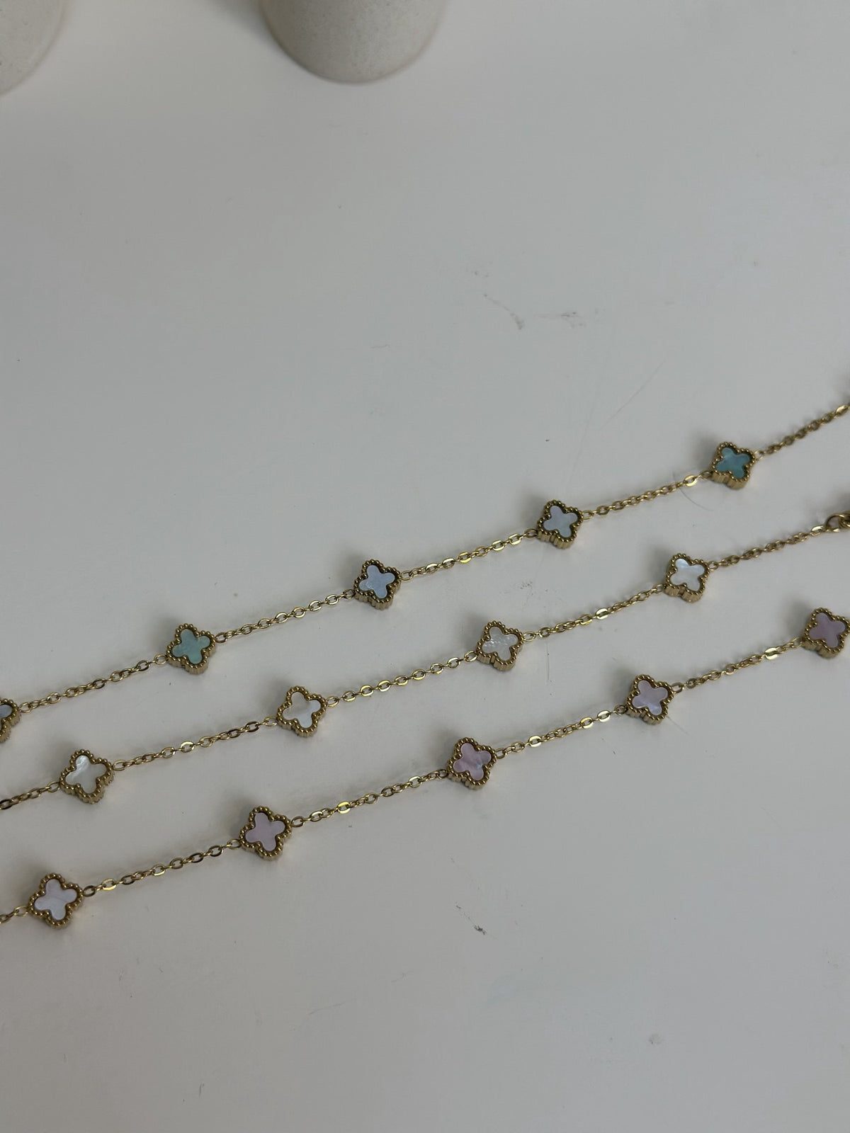 Paired Clover Petite Bracelet in gold-tone, three bracelets laid flat showing pastel clover motifs in different tones