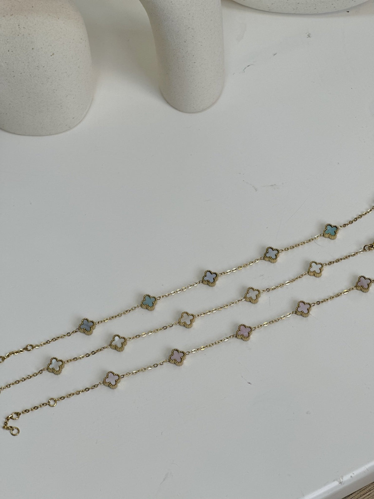 Paired Clover Petite Bracelet in gold-tone, three bracelets laid flat in white, blue and pink clover tones