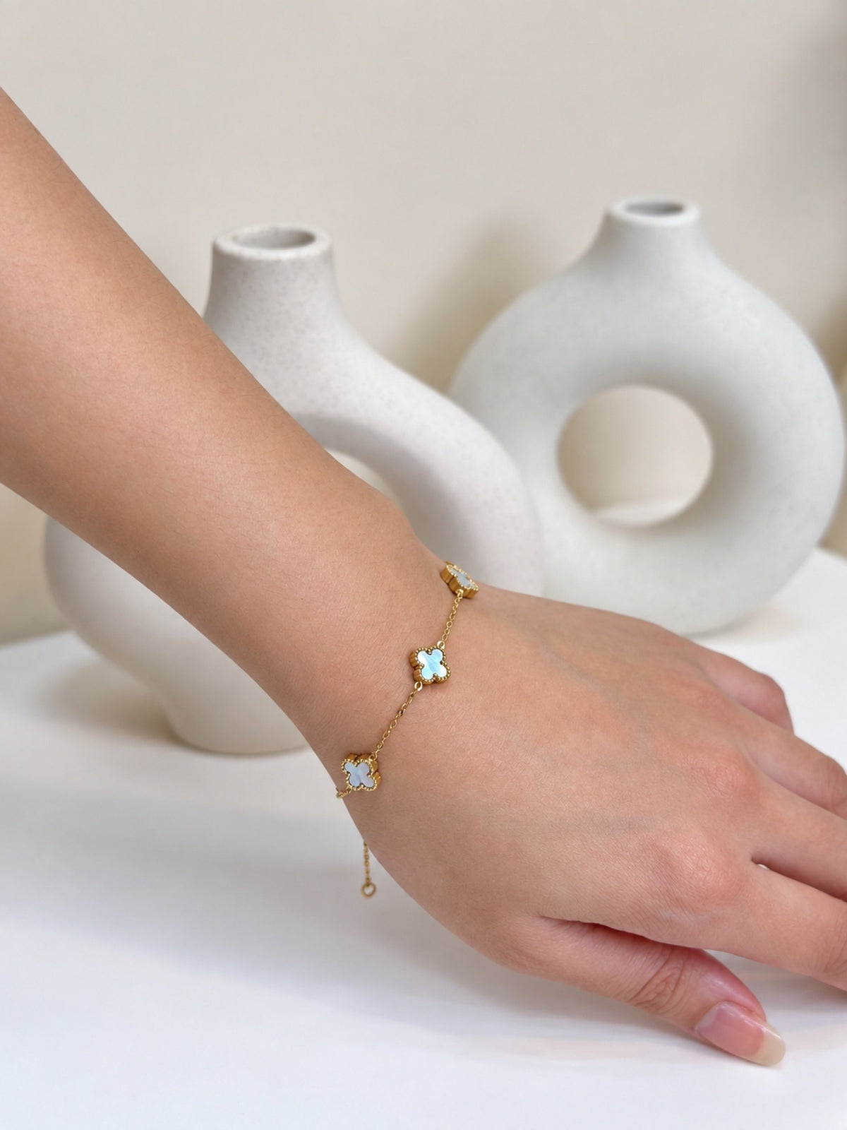 Paired Clover Signature Bracelet in blue, gold-tone chain worn on the wrist with a clover-shaped motif