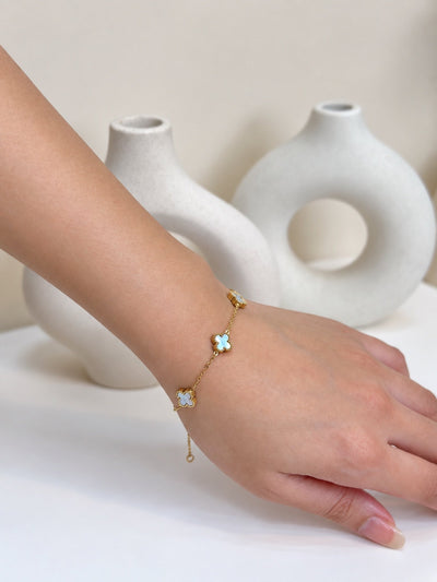 Paired Clover Signature Bracelet in blue, gold-tone chain worn on the wrist with a clover-shaped motif