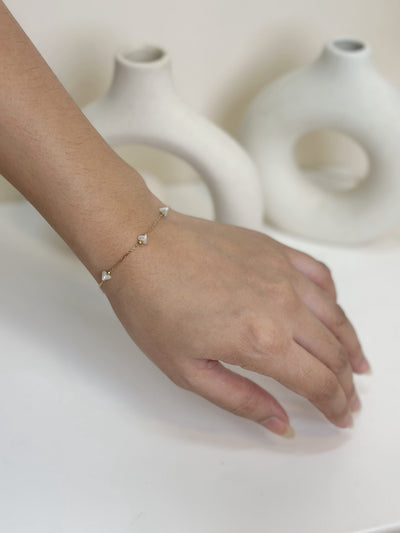 Paired Dorevia Bracelet in gold-tone, worn on the hand with a slim chain and small white heart beads