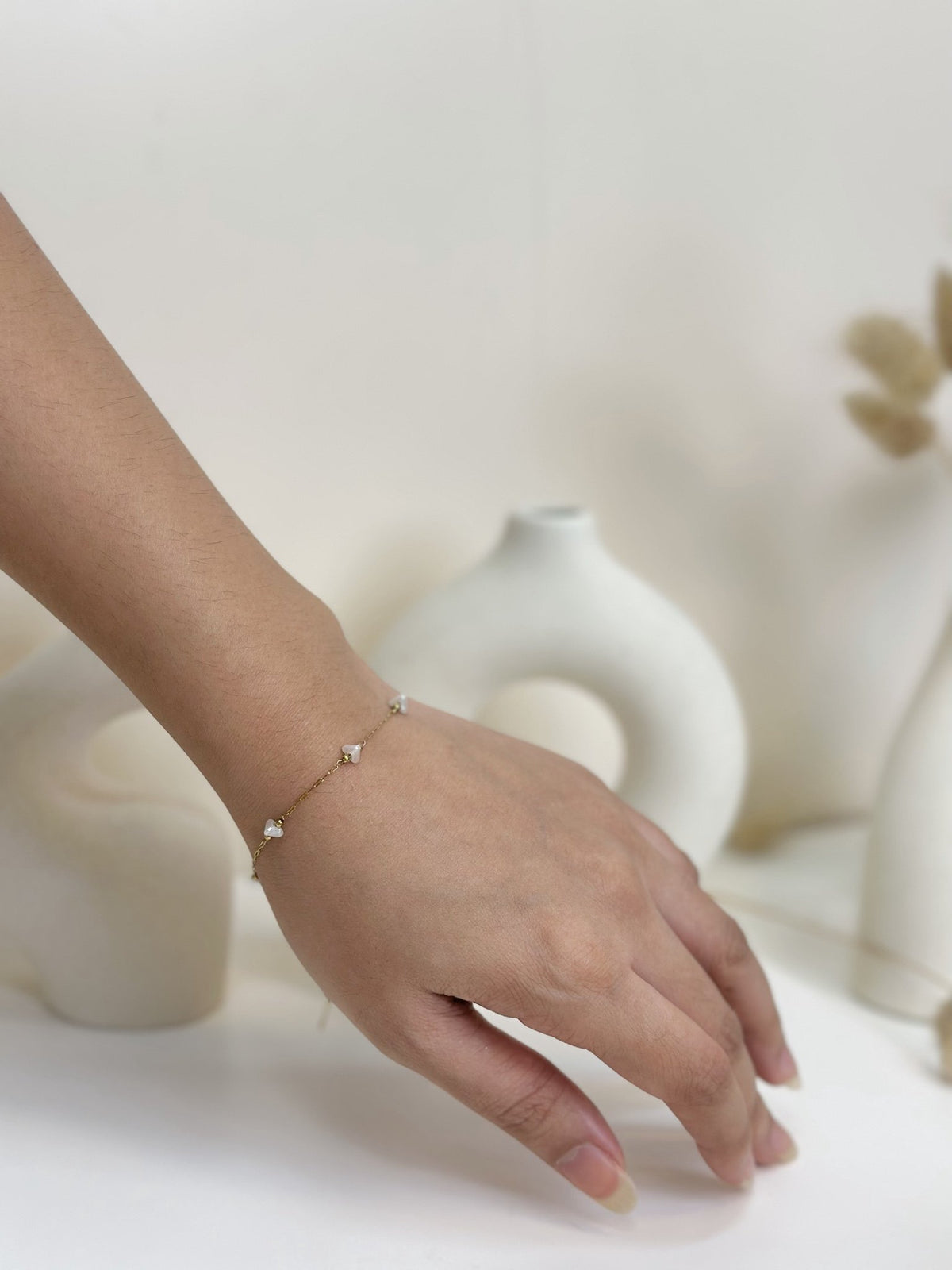 Paired Dorevia Bracelet in gold-tone, worn on the wrist with a slim chain and white heart beads, styled with vases