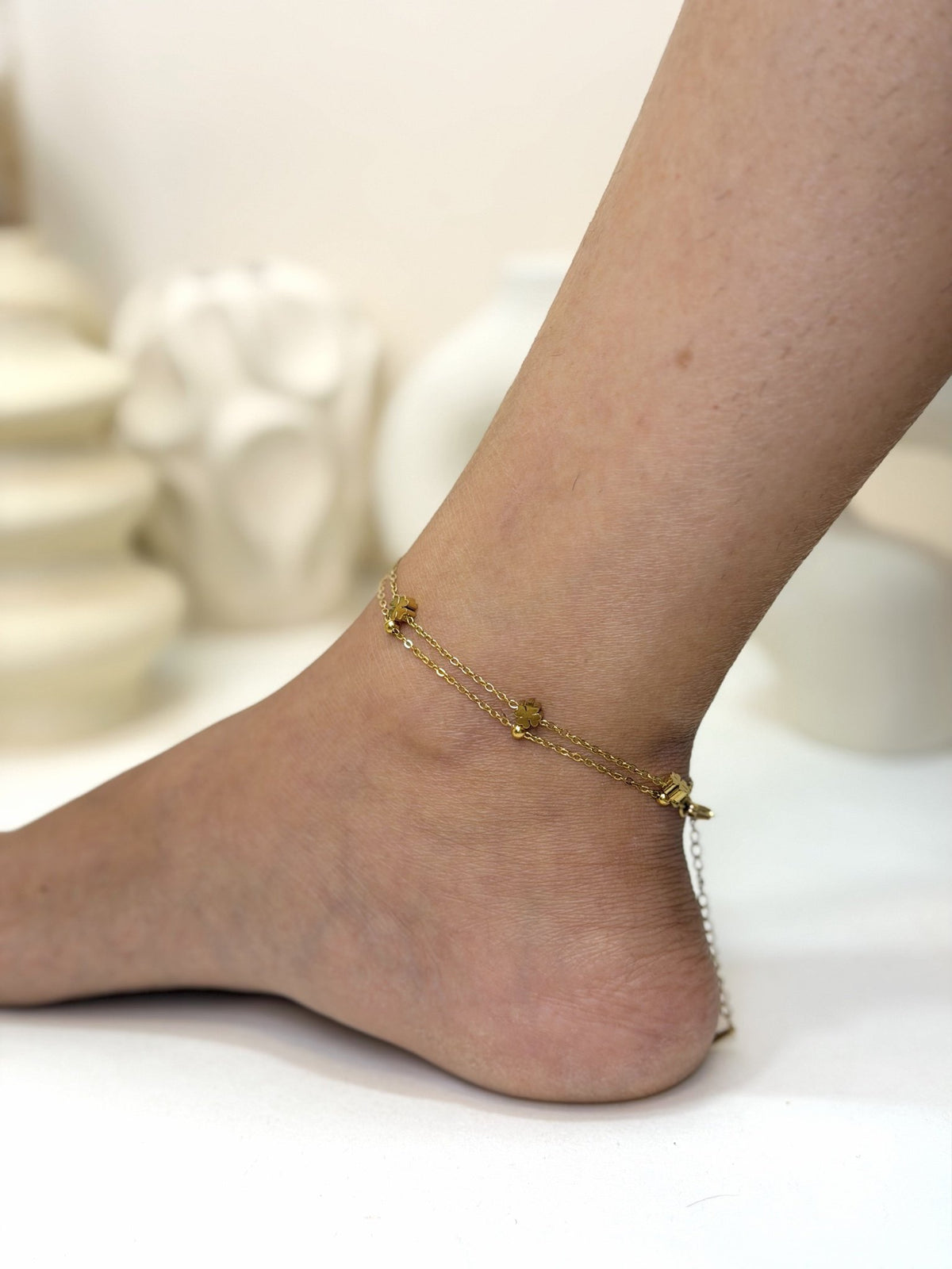 Paired Elara Anklet in gold-tone, worn at the ankle with fine double chains and floral charms