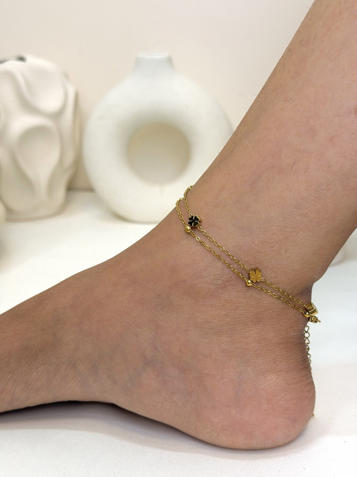 Paired Elara Anklet in gold-tone, worn on the ankle with a double chain and small flower-shaped charms