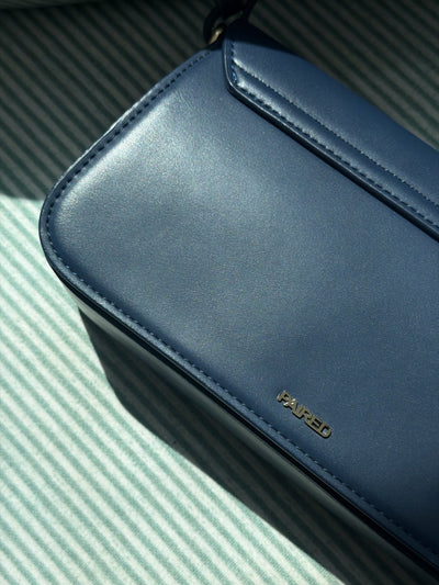Paired Elise Lock Bag in navy blue, close-up of the smooth navy blue corner with the Paired logo on a striped cloth