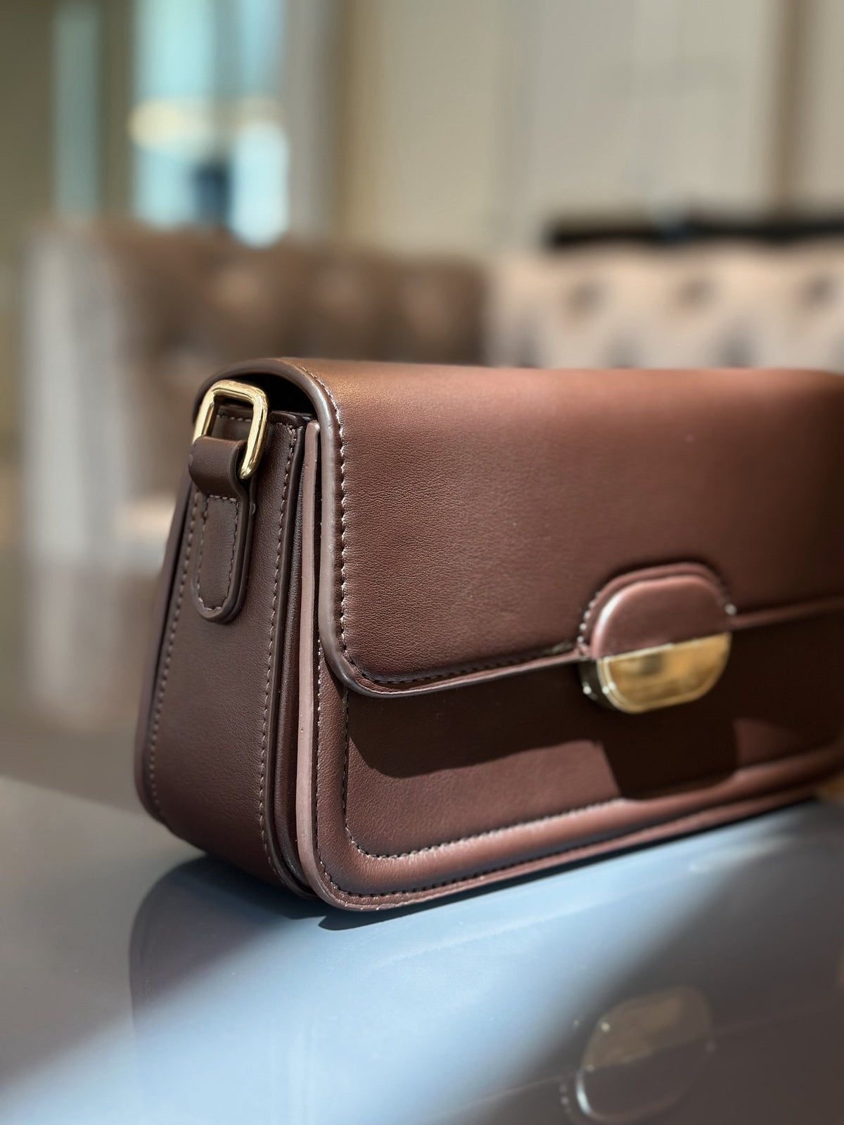 Paired Elise Lock Bag in coffee brown, seen from the side with a smooth flap, gold-tone lock plate and strap buckle