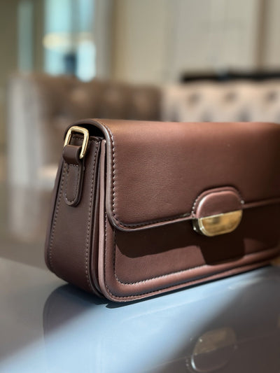Paired Elise Lock Bag in coffee brown, seen from the side with a smooth flap, gold-tone lock plate and strap buckle