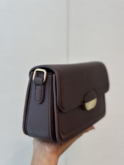 Paired Elise Lock Bag in coffee brown, held in the hand, side view with the strap buckle and gold-tone lock plate