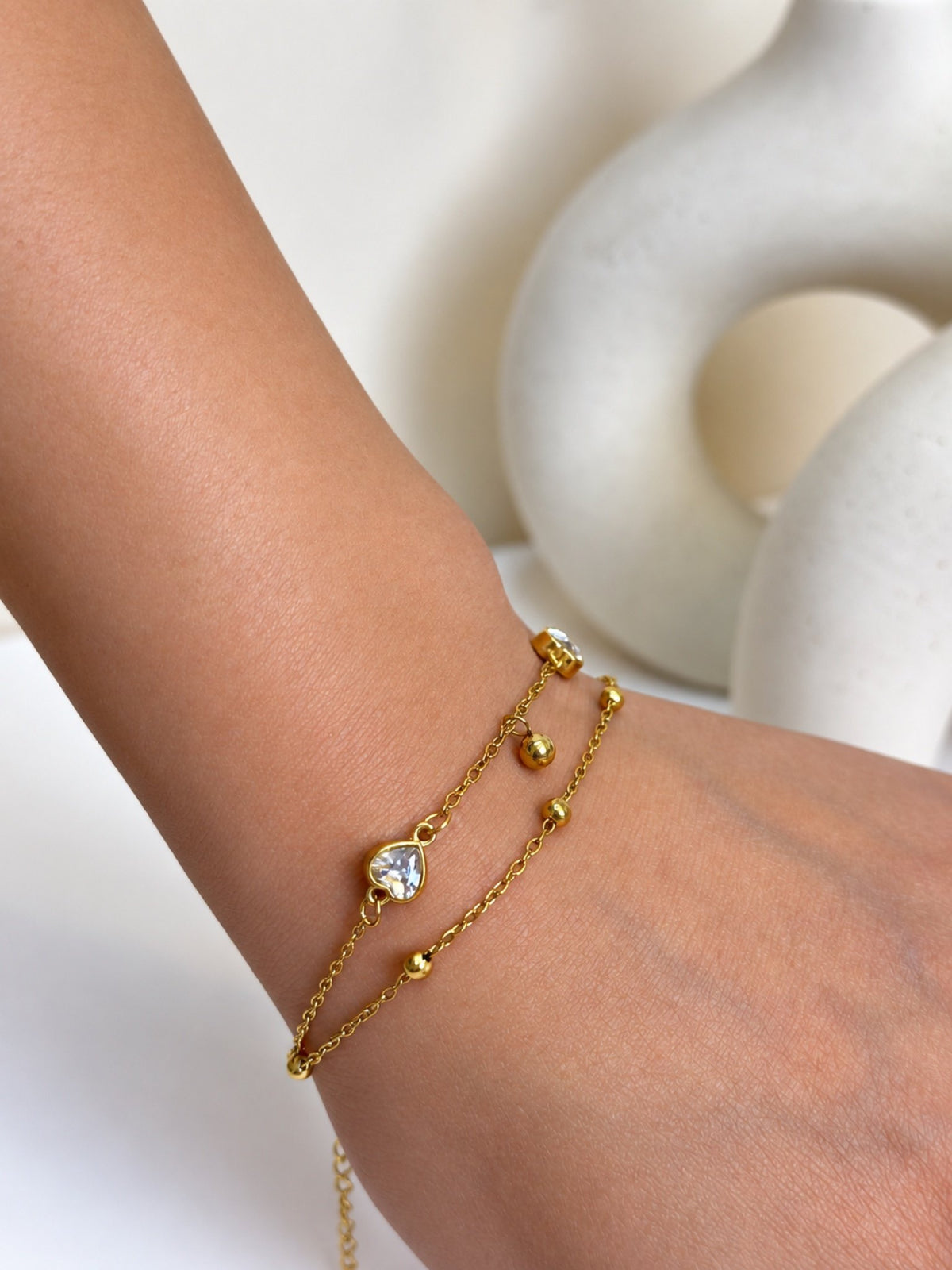 Paired Eliselle Bracelet in gold-tone, close view on the wrist showing the clear heart stone and two beaded chains