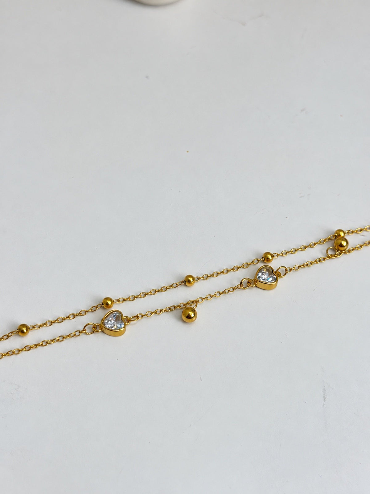 Paired Eliselle Bracelet in gold-tone, flat close-up of the double chain with clear heart stones and round beads