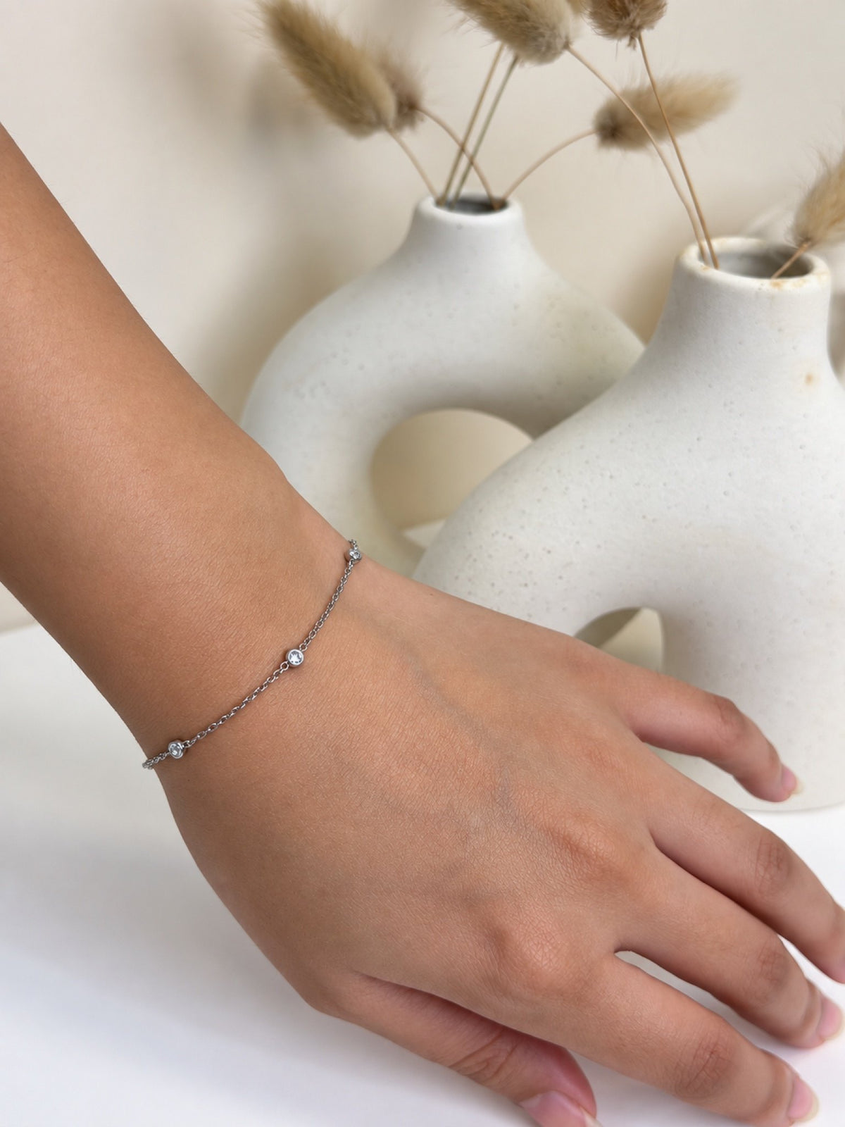 Paired Isabelle Bracelet in silver-tone, worn on the wrist with a slim chain and small clear stones