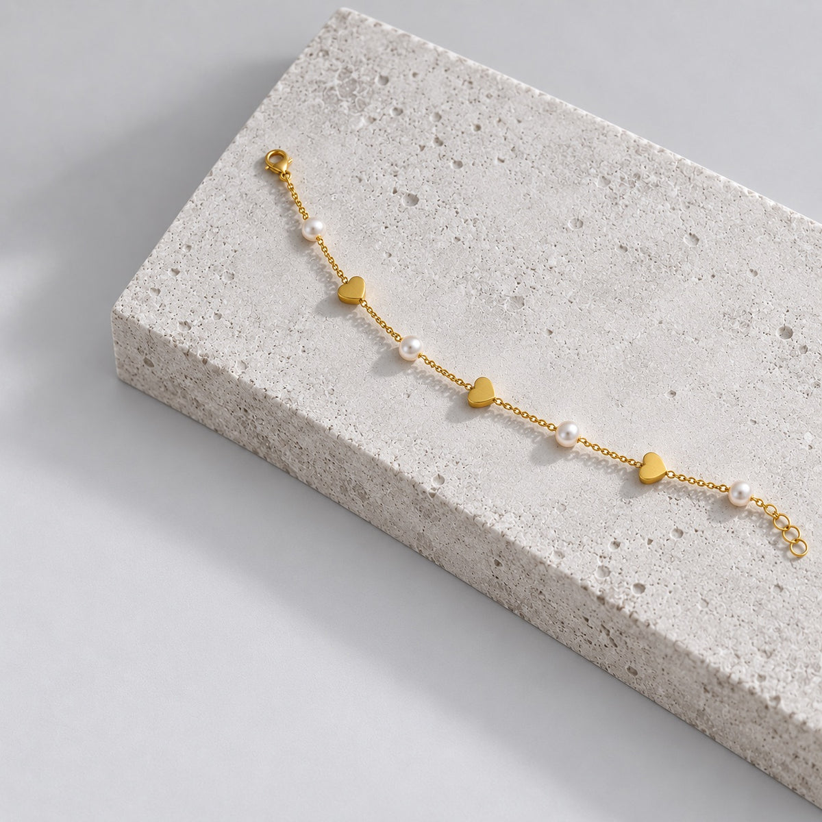 Paired gold heart charm bracelet on a grey stone plinth