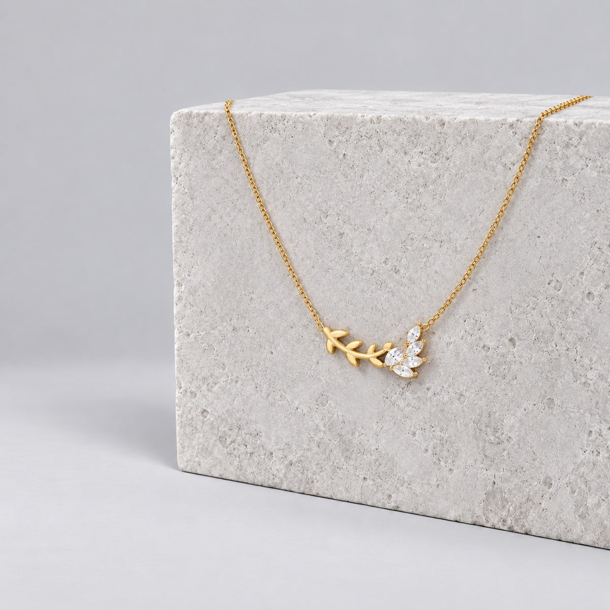 Paired gold leaf pendant necklace on a grey stone plinth