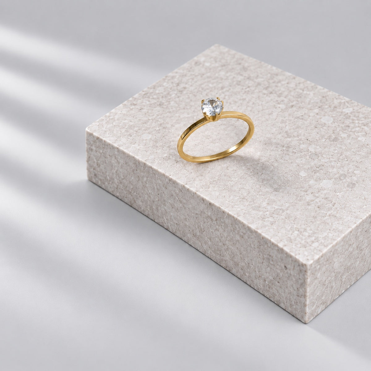 Paired gold solitaire ring on a grey stone plinth