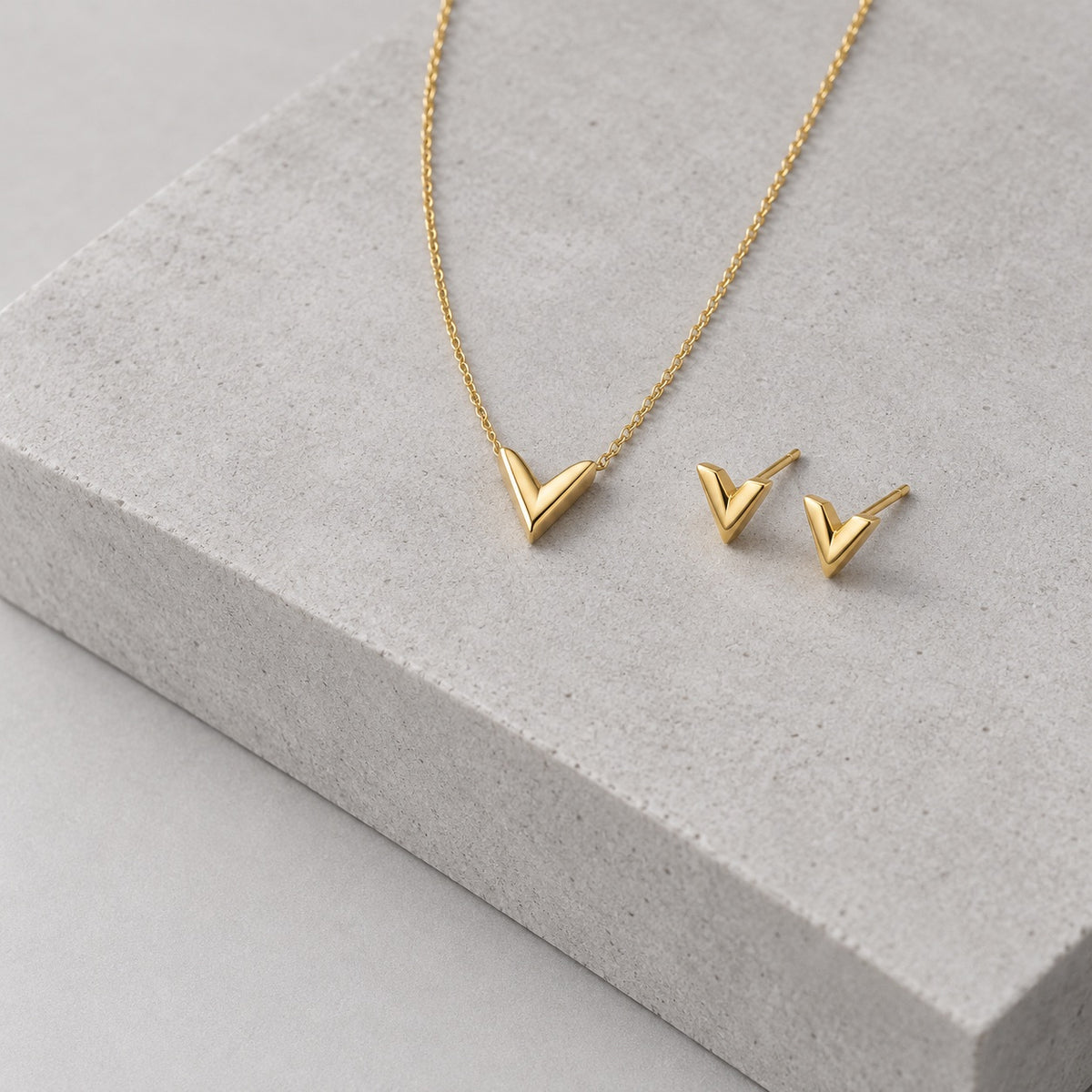 Paired gold chevron necklace and earrings set on grey stone