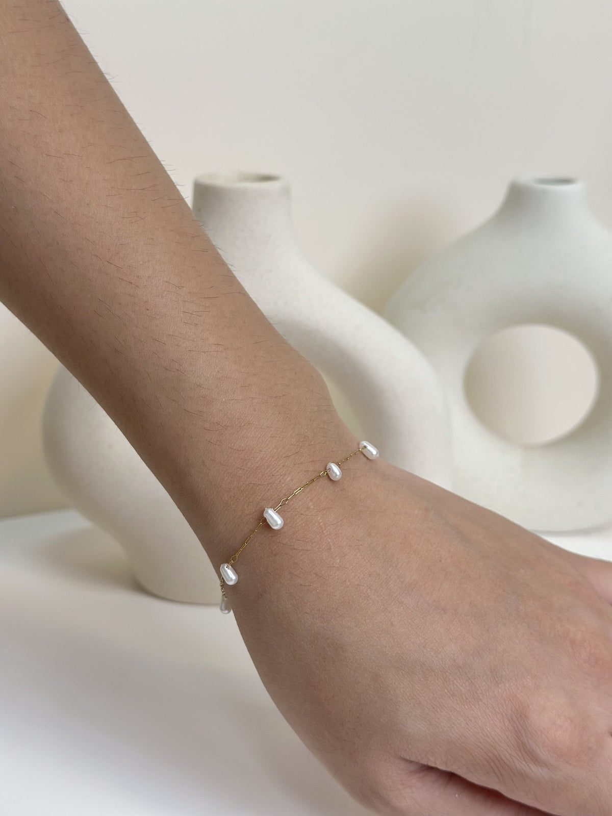 Paired Laurentia Bracelet in gold-tone, close view on the wrist showing white oval beads along a fine chain