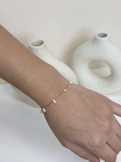 Paired Laurentia Bracelet in gold-tone, worn on the wrist and hand with white oval beads on a fine chain