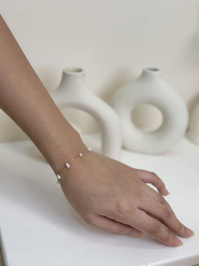 Paired Laurentia Bracelet in gold-tone, worn on the wrist with a very fine chain and small white oval beads