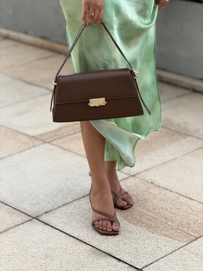 Paired Liora Frame Bag in coffee brown, carried by a slim strap in the hand beside a green satin skirt