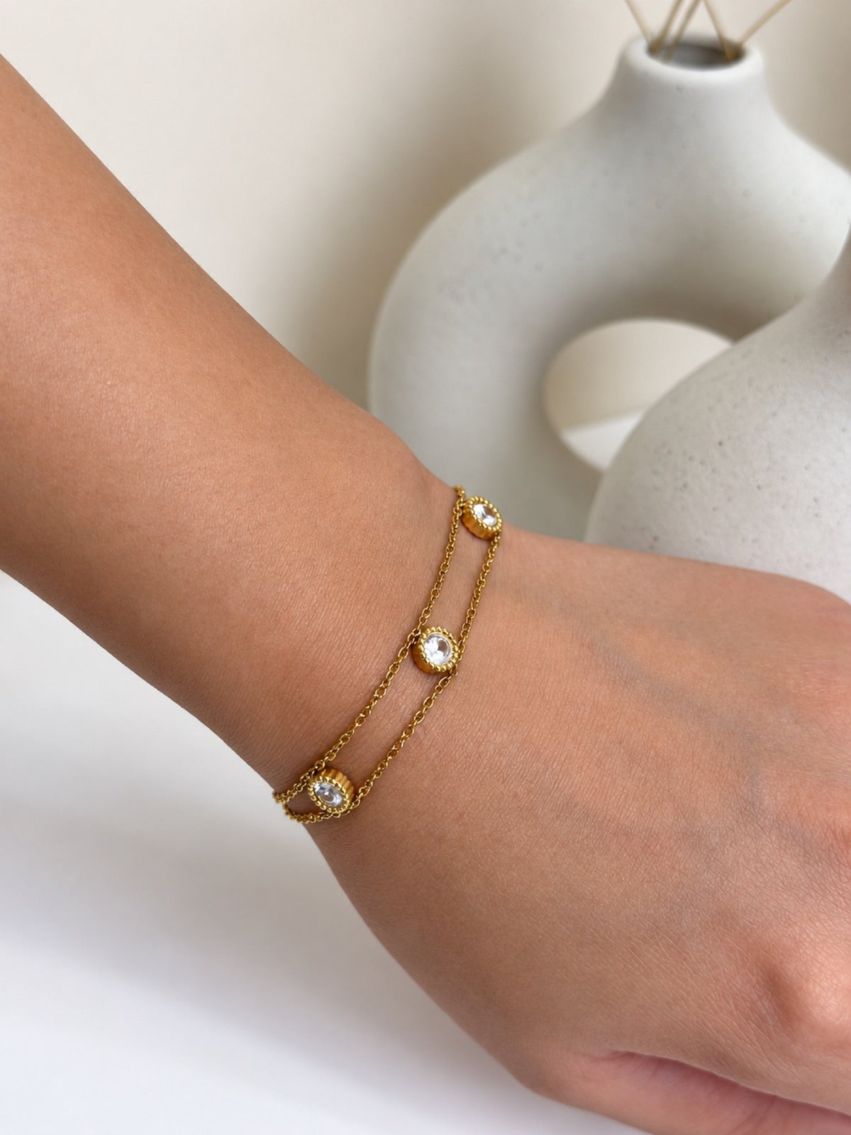 Paired Lisandra Bracelet in gold-tone, close view on the wrist showing a double chain with round clear stones