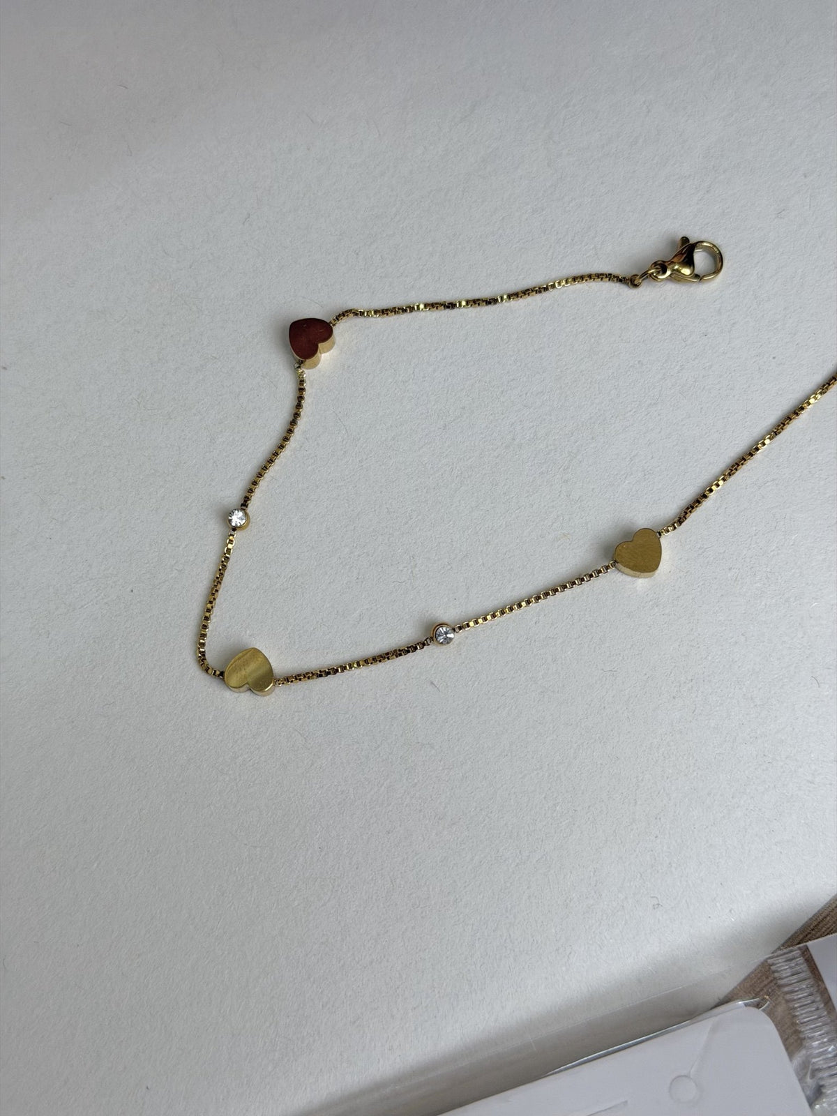 Paired Lorielle Anklet in gold-tone, laid flat showing the fine chain, heart charms, clear stones and lobster clasp