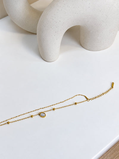 Paired Melisande Bracelet in gold-tone, laid flat on white showing a double chain, tiny beads, oval charm and clasp