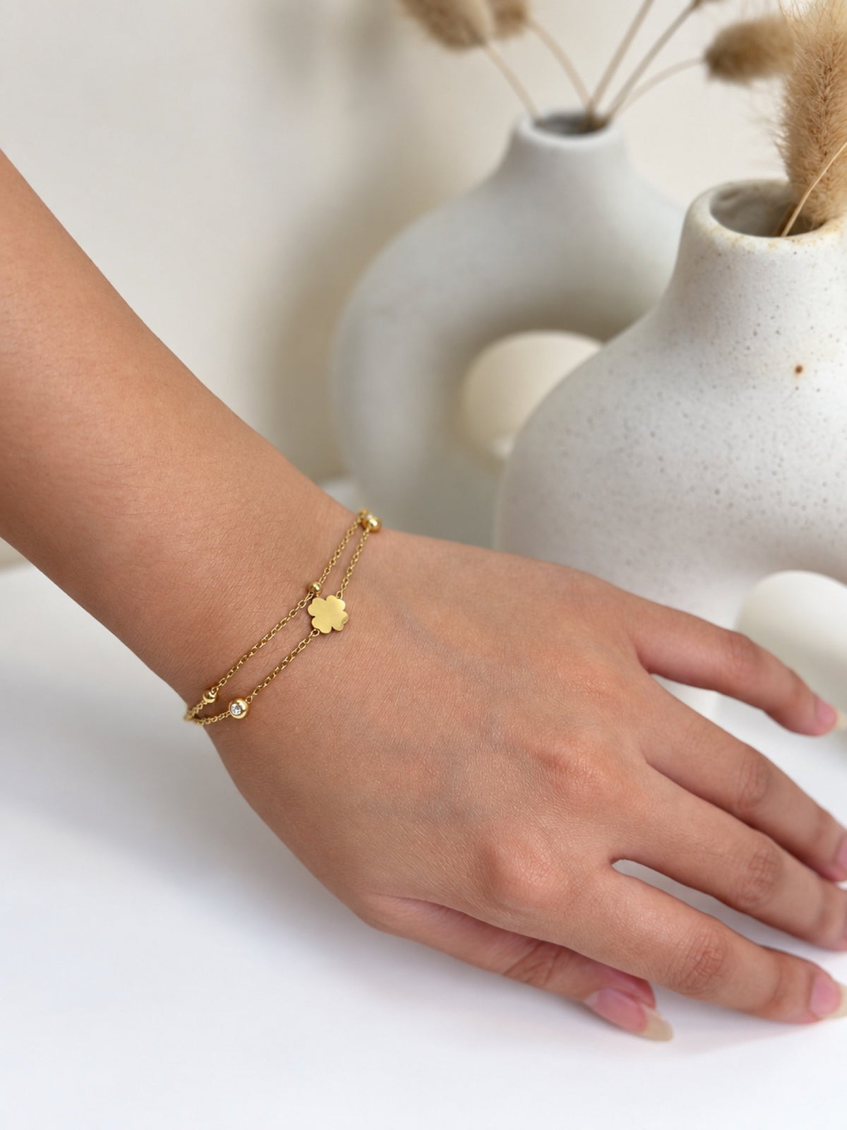 Paired Nimoria Bracelet in gold-tone, side view on the wrist showing two fine chains and a small clover charm