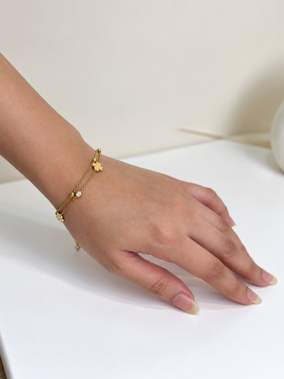 Paired Nimoria Bracelet in gold-tone, worn on the wrist with a double chain, a small clover charm and a clear stone