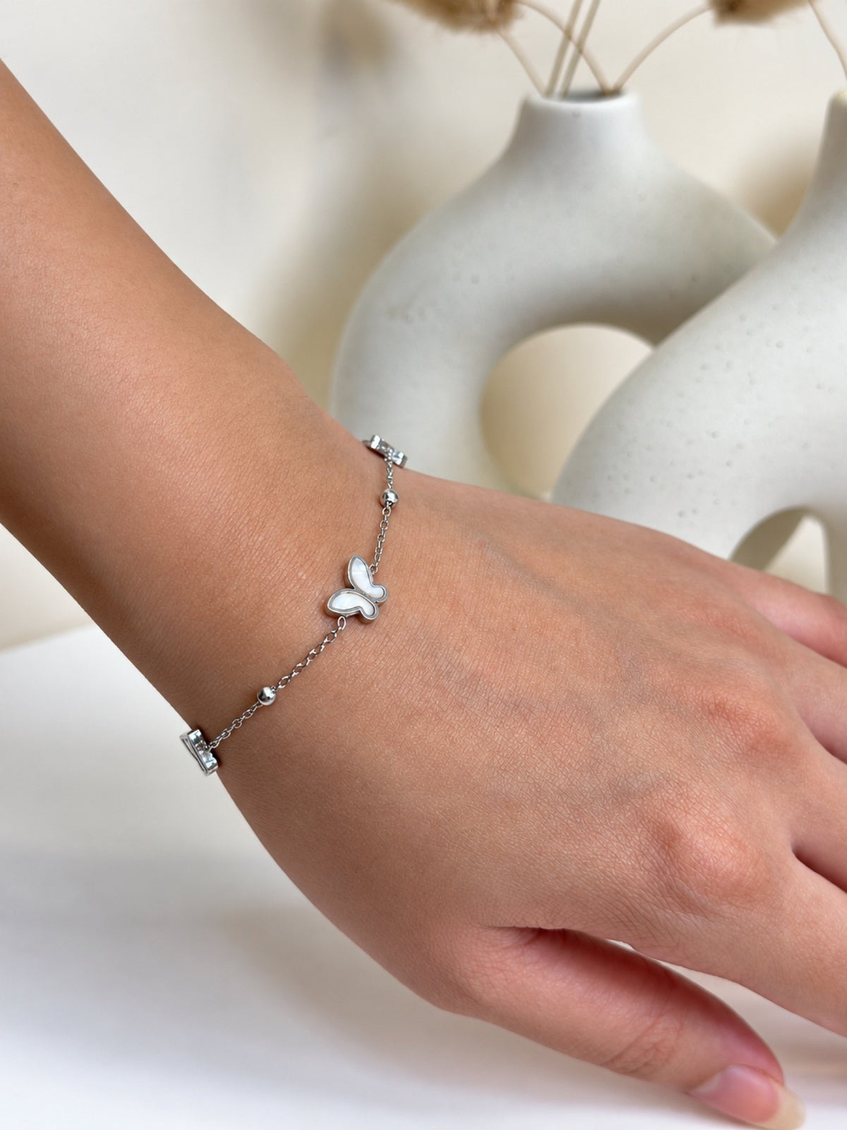 Paired Odelisse Bracelet in silver-tone, worn on the wrist with a fine beaded chain and a single silver butterfly charm