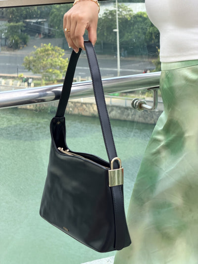 Paired Oriana Gold-Lock Bag in black, held by its strap with a gold-tone side detail, photographed sideways