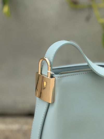 Paired Oriana Gold-Lock Bag in soft blue, close-up of the gold-tone padlock charm and curved strap