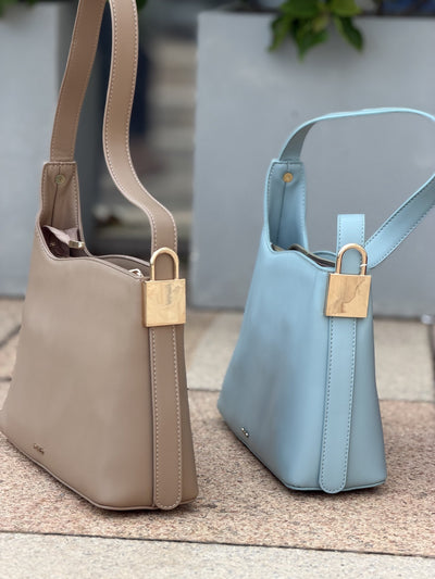 Paired Oriana Gold-Lock Bag in taupe and soft blue, standing together with gold-tone padlock charms at the side