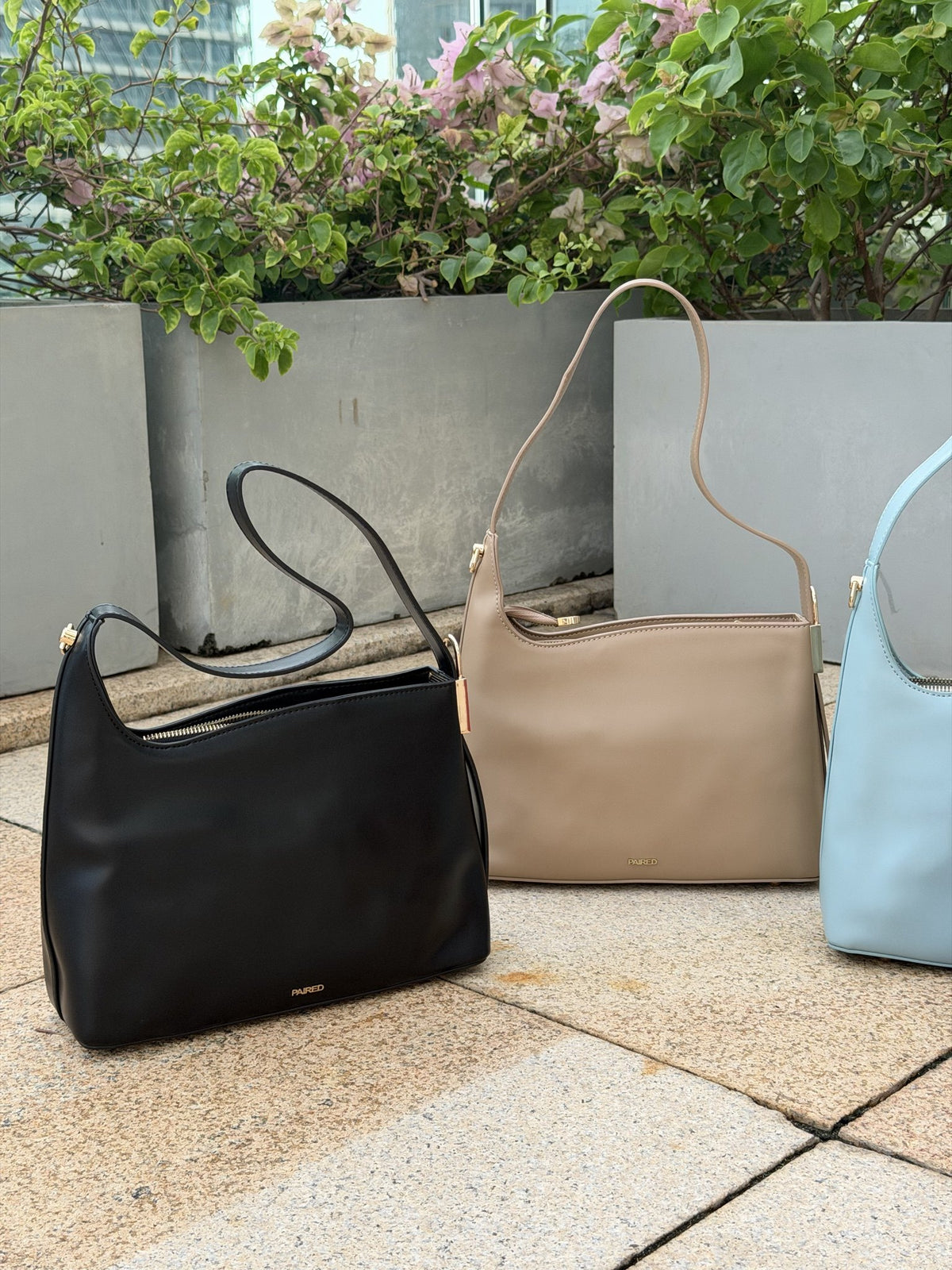 Paired Oriana Gold-Lock Bag in soft blue, taupe and black laid out on stone paving, photographed sideways