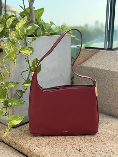 Paired Oriana Gold-Lock Bag in red, a relaxed shoulder bag with a curved strap and gold-tone side detail on a stone ledge