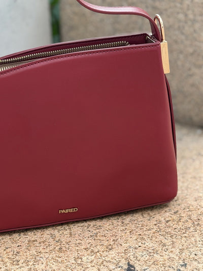 Paired Oriana Gold-Lock Bag in red, close-up of the smooth front, gold-tone side detail and logo at the base