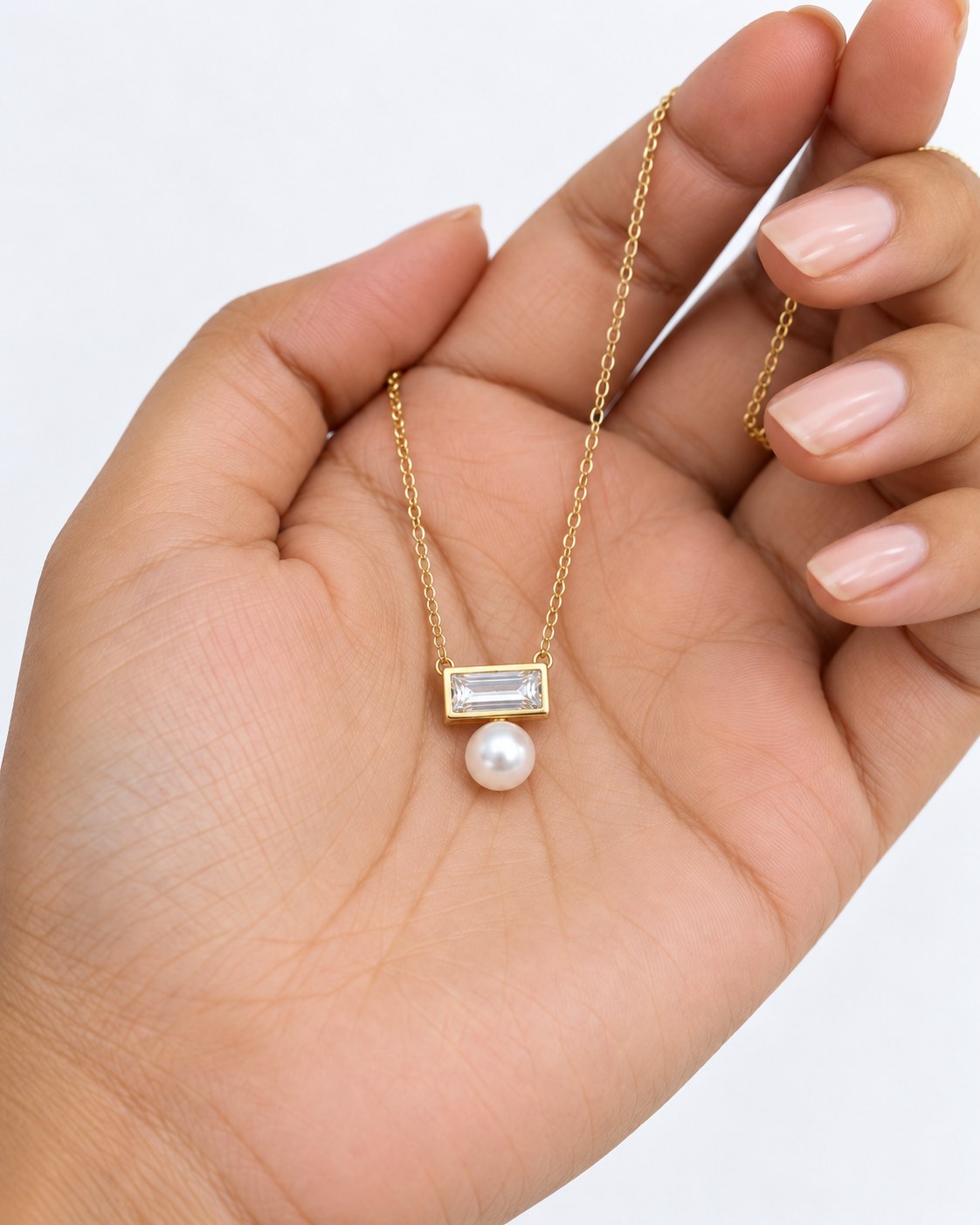 Paired Radiant Love Chain in gold-tone, pendant in the palm: clear baguette crystal bar with a pearl hanging below