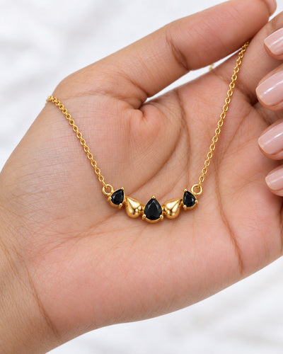 Paired Raven Drops Chain in black, pendant in the palm showing three black pear stones and two gold-tone drops
