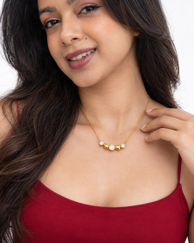 Paired Raven Drops Chain in white, worn close-up on the neckline with clear pear stones and gold teardrops