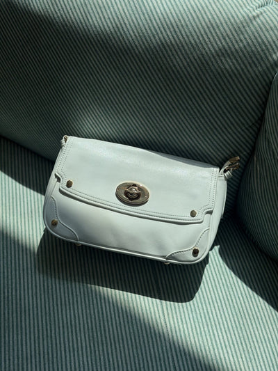 Paired Riviera Lock Bag in pale mint, with a flap, gold-tone turn-lock and studded corners, lying on a green striped cushion