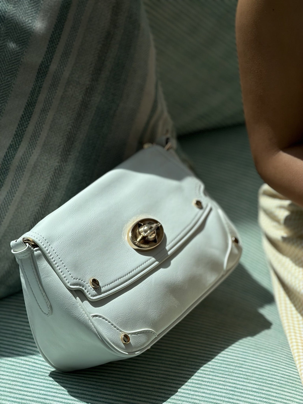 Paired Riviera Lock Bag in pale mint, with a gold-tone turn-lock and soft flap, resting at an angle on a striped sofa