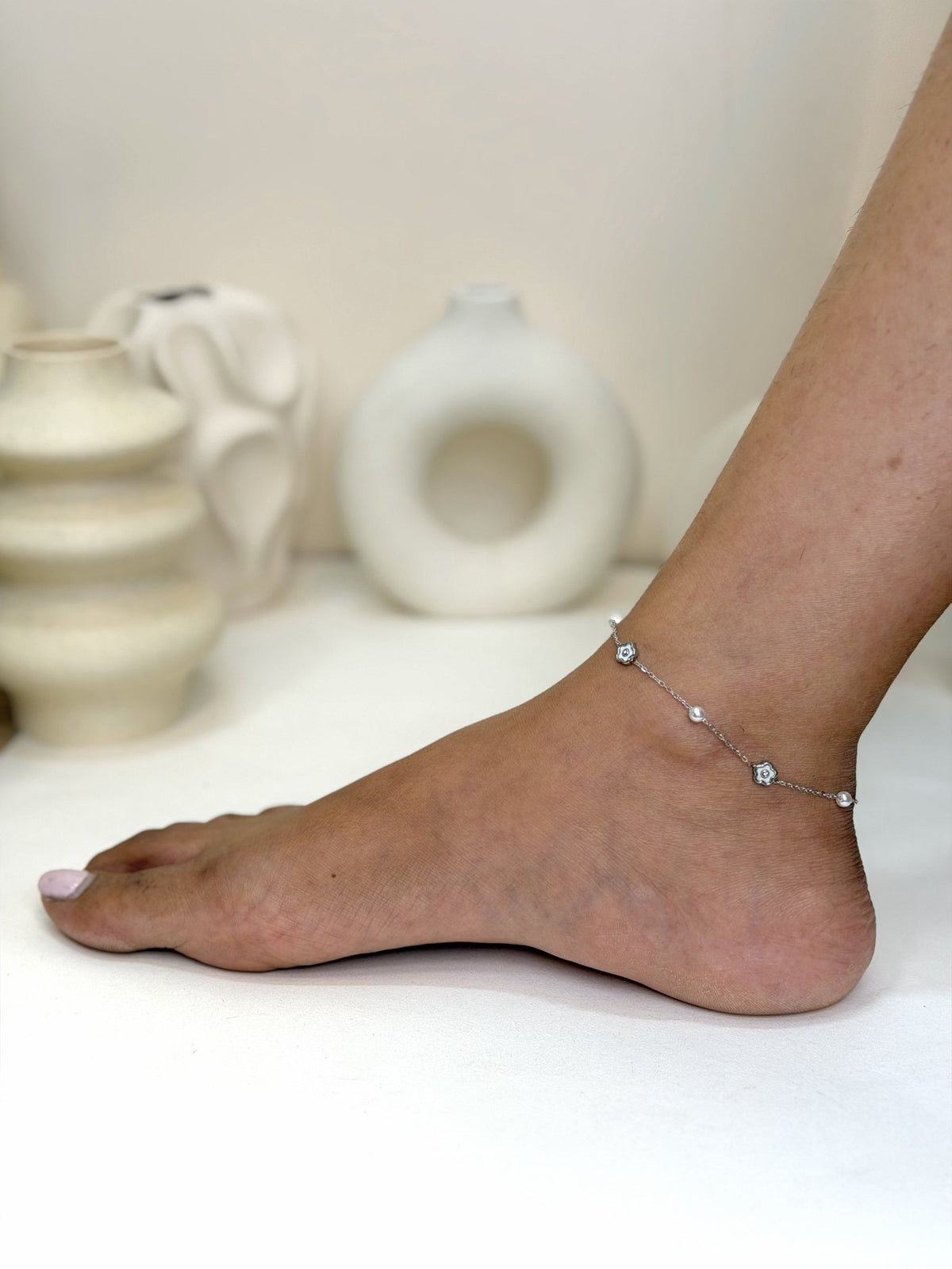 Paired Rosalie Anklet in silver-tone, worn on the foot and ankle with spaced flower stones and white beads