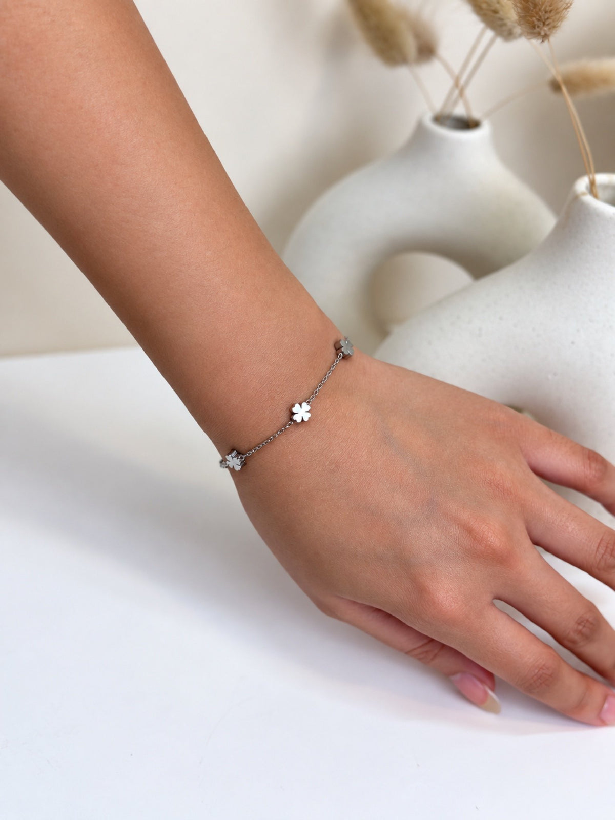 Paired Saphielle Bracelet in silver-tone, worn on the wrist with a slim chain and small four-petal clover charms