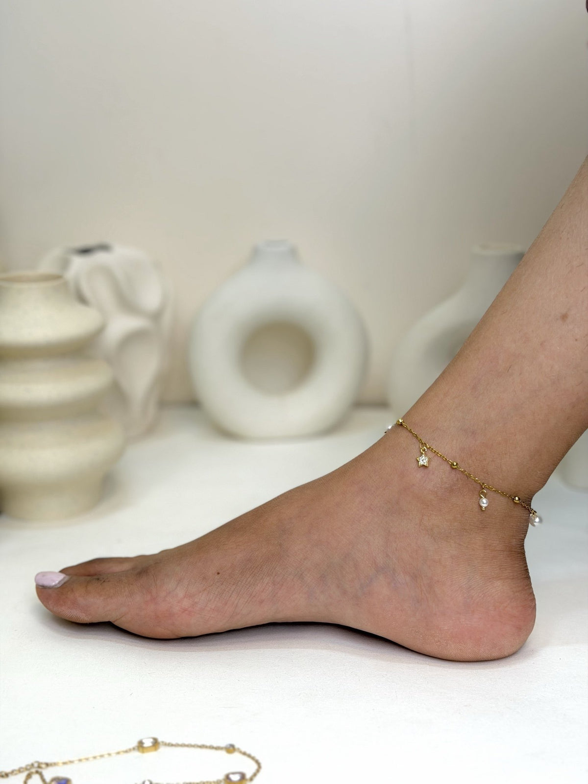 Paired Serelle Anklet in gold-tone, worn on the foot and ankle with a beaded chain and small charms