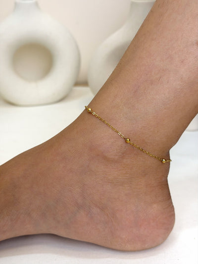 Paired Solène Anklet in gold-tone, worn on the ankle with a fine chain and small ball beads