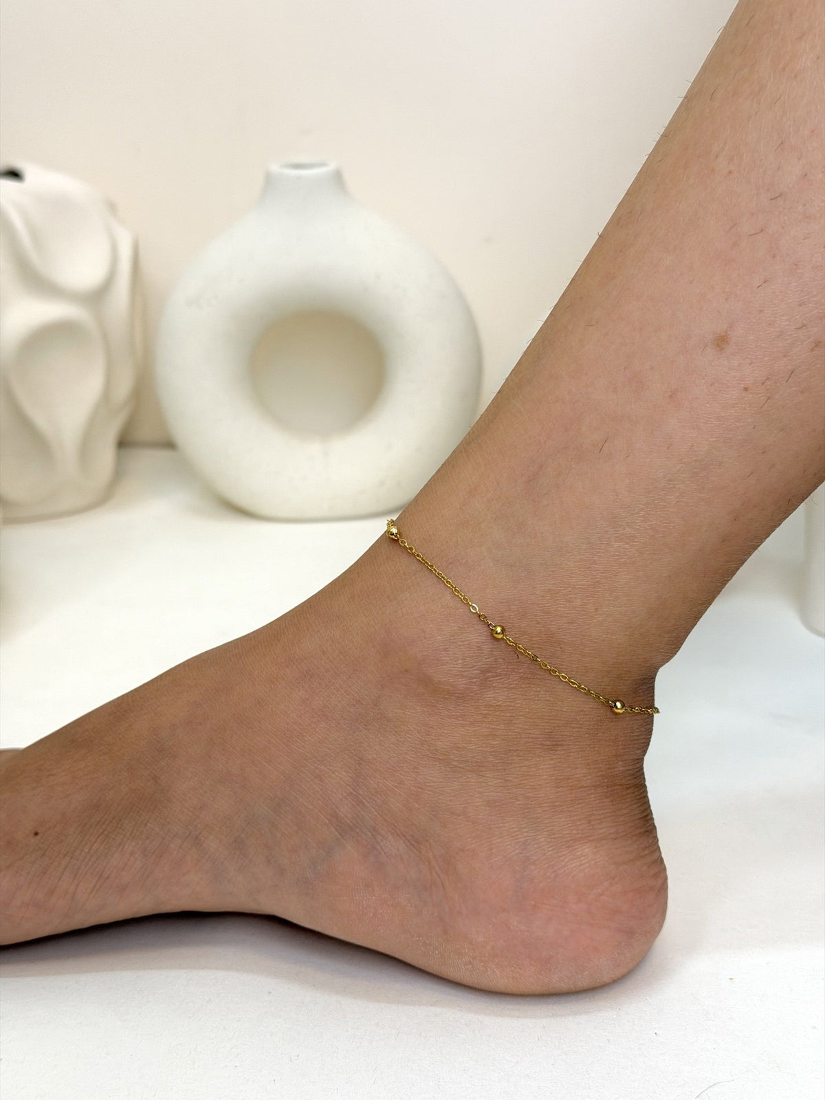 Paired Solène Anklet in gold-tone, side view on the ankle with a fine chain and small ball beads