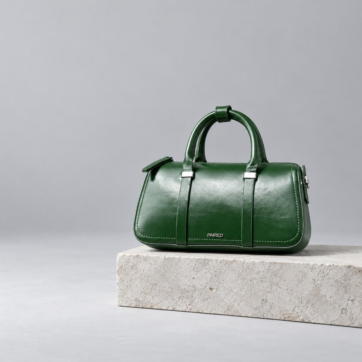 Green Paired Ivy Box Bag with rolled top handles on a pale stone plinth